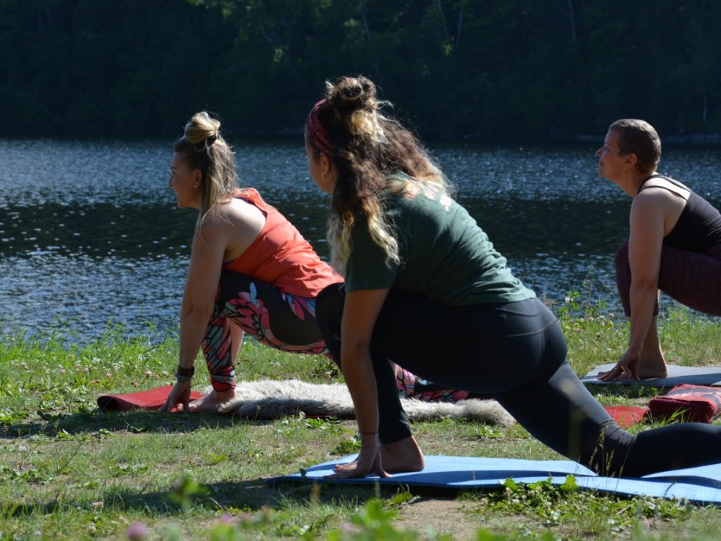 3 personnes faisant du yoga à l'extérieur sur le bord de l'eau dans le gazon
